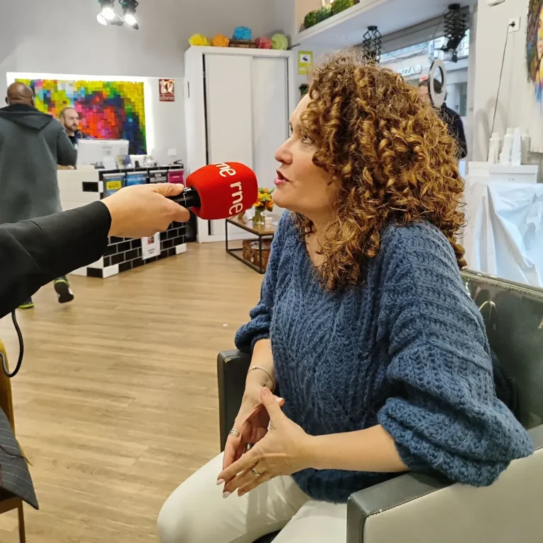 Mujer con cabello rizado hablando en una entrevista, en un entorno artístico y colorido.
